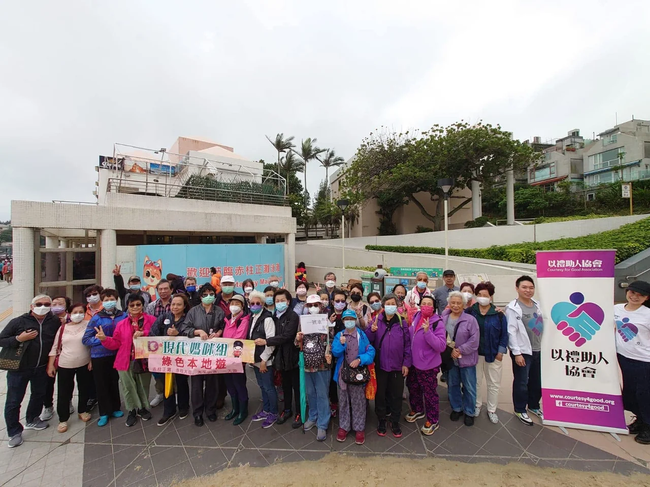 長者與義工戶外合照；背景可見赤柱正灘標示及以禮助人協會易拉架。
